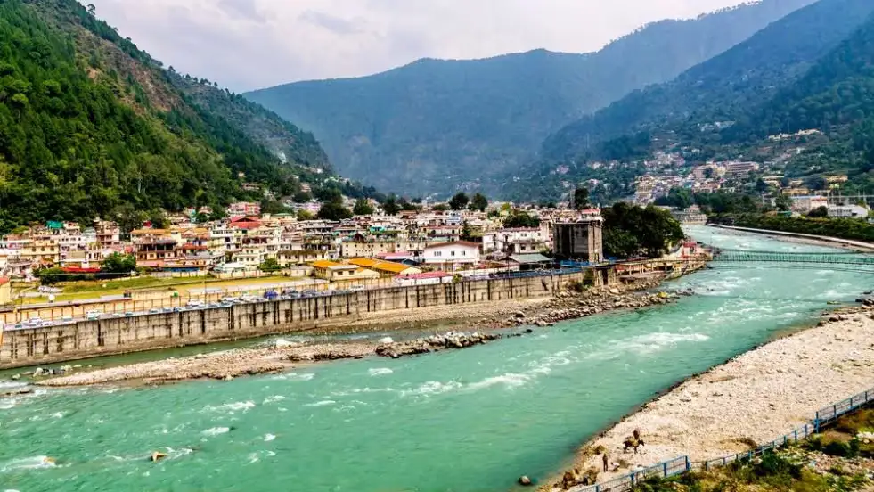 Kashi Vishwanath Temple in Uttarkashi, Uttarakhand—an ancient Himalayan-style stone temple with traditional sloping roofs and wooden beams, set against a backdrop of mist-covered mountain ridges by the Bhagirathi River.