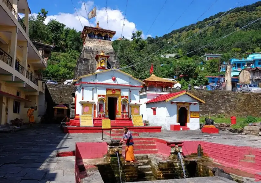 Kashi Vishwanath Temple in Uttarkashi, Uttarakhand, India—an ancient Hindu temple with a white and red facade, tall stone Shikhara spire, and a sacred courtyard water tank against lush green mountains.