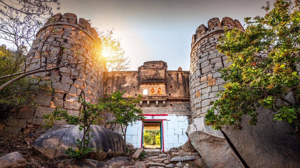A low-angle shot of the historic stone gateway and stone bastions at Anegundi near Hampi, with the sun gleaming brightly from behind the ancient fort walls.