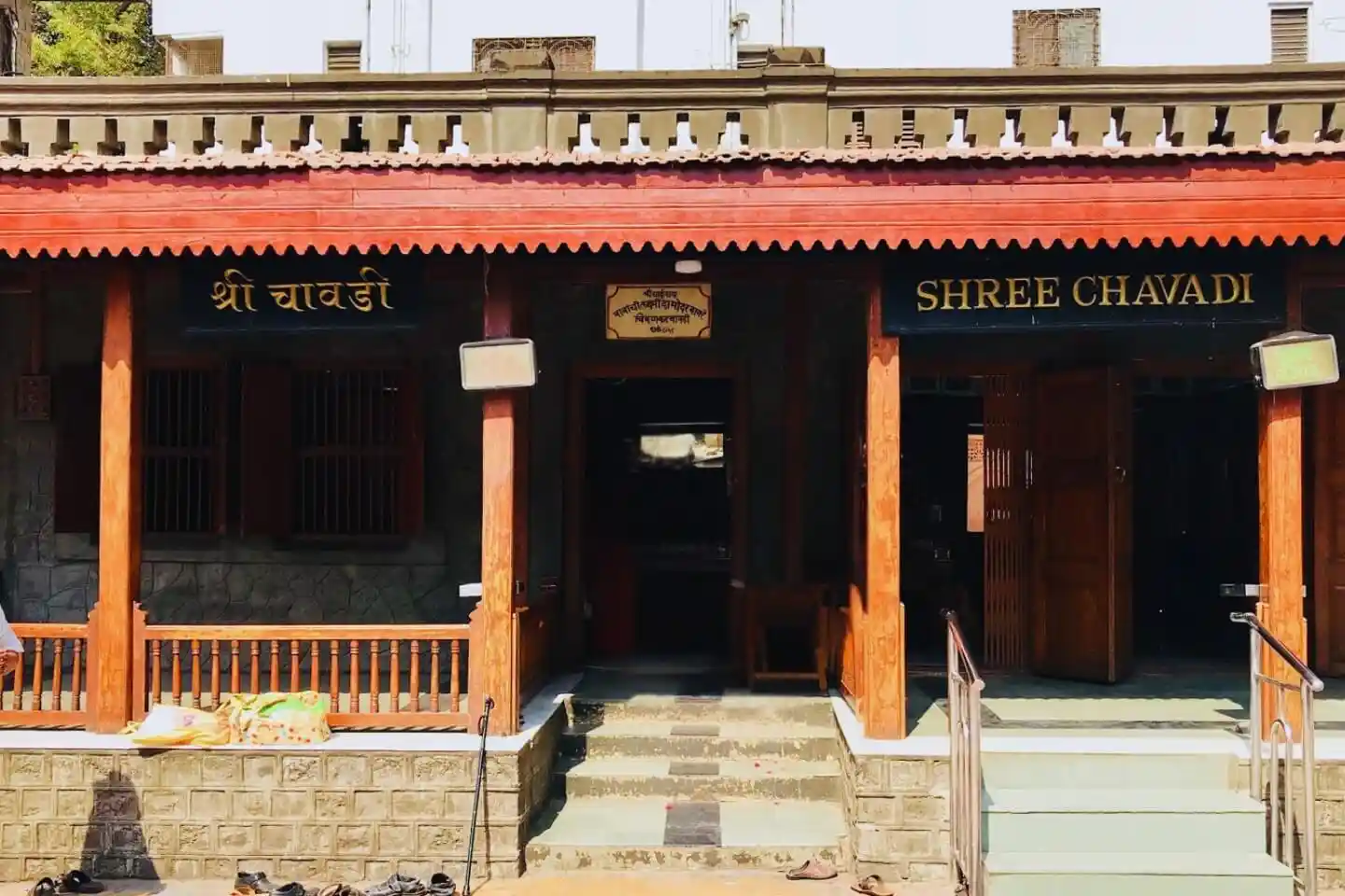 The front exterior facade of the Shree Chavadi building in Shirdi, featuring dark wood pillars, a decorative tiled roof awning, and prominent black signs reading "श्री चावडी" in Devanagari script and "SHREE CHAVADI" in English.