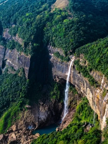 High-angle vertical view of the iconic Nohkalikai Waterfall plunging down a rocky cliff into a blue pool in Cherrapunji, Meghalaya tourism.